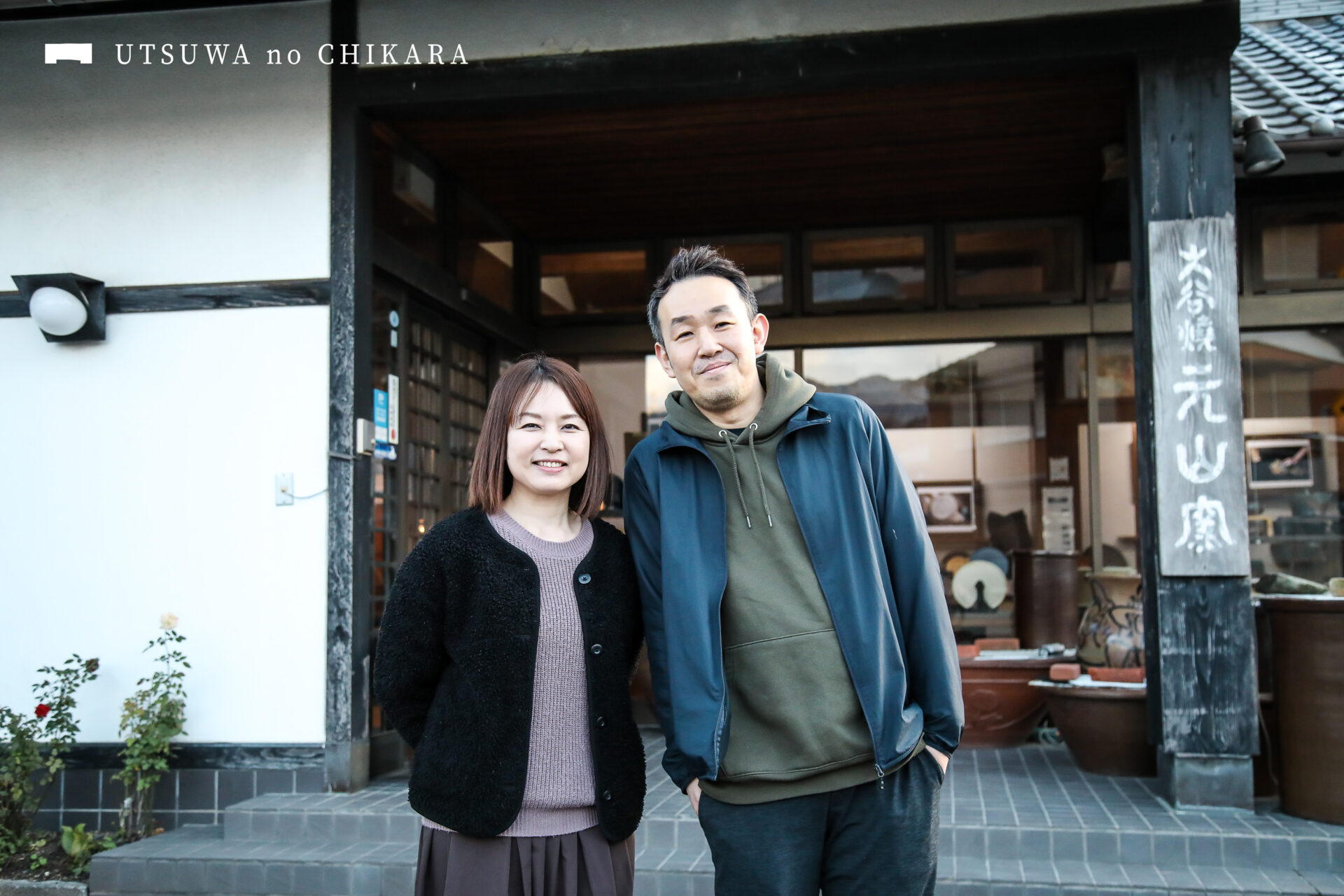 十代の重みを感じる看板を携えるギャラリーの前で。田村さんと奥様の景子さん。仲良しなお二人に癒されます。
